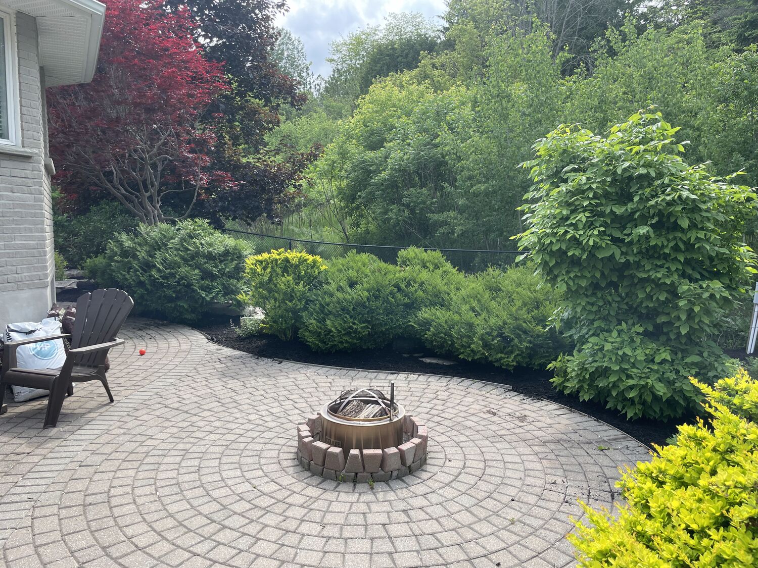 Circular paver patio with a stone fire pit and layered hedges